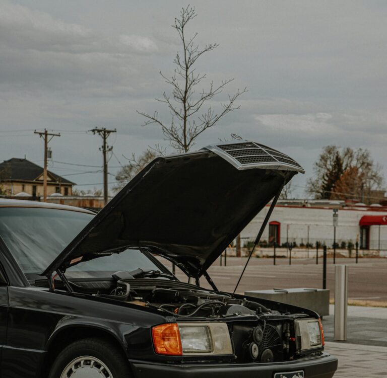 A classic black Mercedes Benz parked with its hood open in an urban environment.